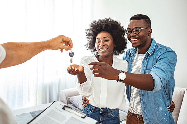 Photo of a smiling young couple thanking to the agent for the new house. Homeowners receiving their new house keys.