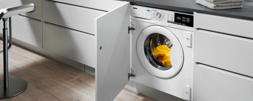 Zanussi washing machine in built into kitchen cabinet with fluffy yellow towel inside.