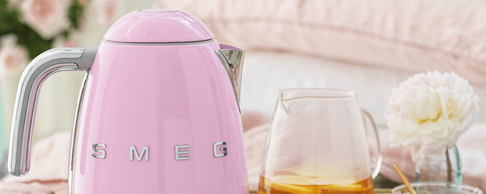 Baby pink Smeg kettle next to a jug of tea and a flower table decor.