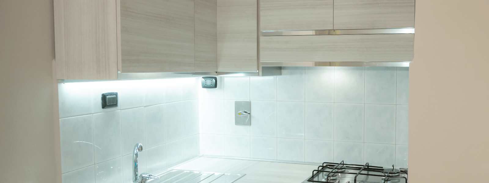 White under-cabinet lighting shown in kitchen with white splashback and light wood cabinets.