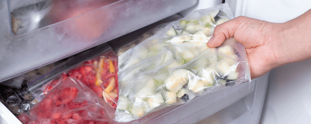 Hand removing a clear bag of frozen vegetables from a freezer drawer