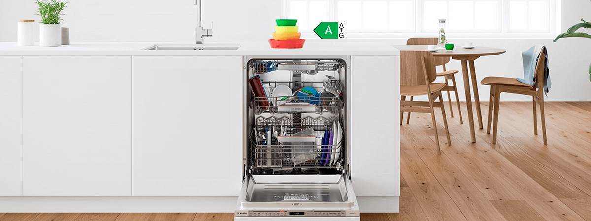 An open dishwasher integrated into white cabinets, with an energy rating label showing A-G