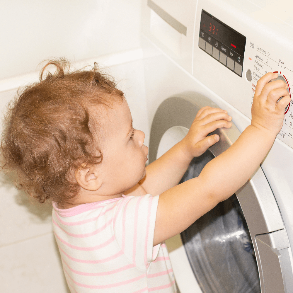 Toddler playing with washing machine dial.