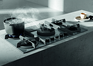 An Elica NikolaTesla Flame air venting gas hob finished in grey featuring a boiling pot of water. The steam from the pot is being drawn to the middle of the hob. Situated in a modern, light grey kitchen.