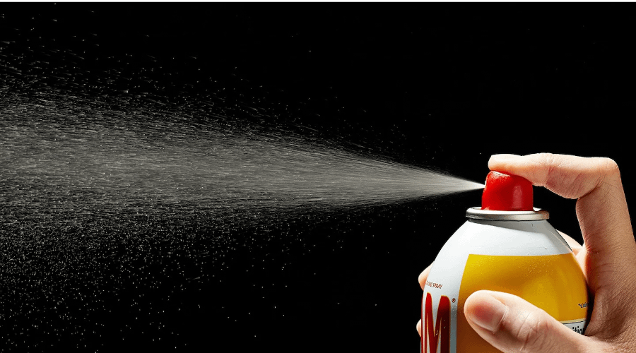 Person spraying cooking oil into the air, with a black background.