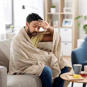 Sick man wrapped in blanket, checking temperature with hand