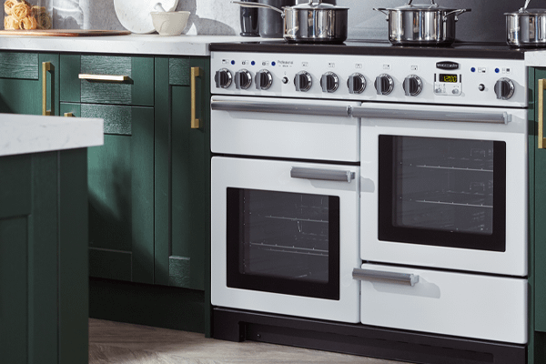 A white Rangemaster range cooker with an induction cooker top, in a emerald green kitchen