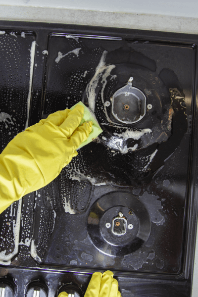 A yellow gloved hand cleaning a black gas hob