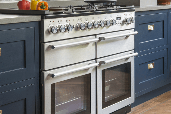A Rangemaster dual fuel range cooker in ivory, set in a blue kitchen