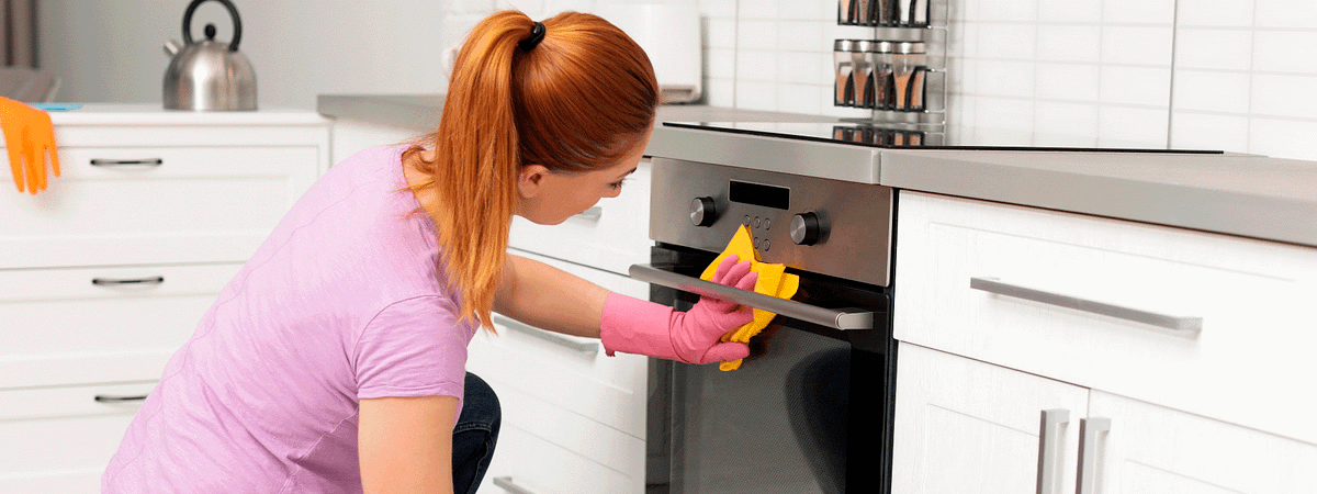 Woman in pink top and gloves cleaning the front of an oven.