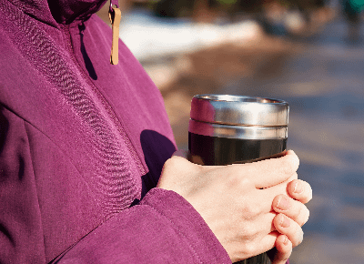 Close up of person in hot pink jacket holding a travel mug with both hands. 