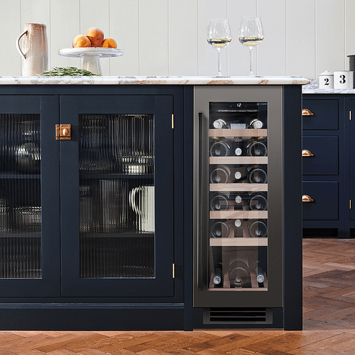 A narrow wine cooler full of wine bottles built into the end of blue cabinetry.