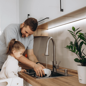 Father showing daughter how to wash up. Under-cabinet lighting is shown in the background.