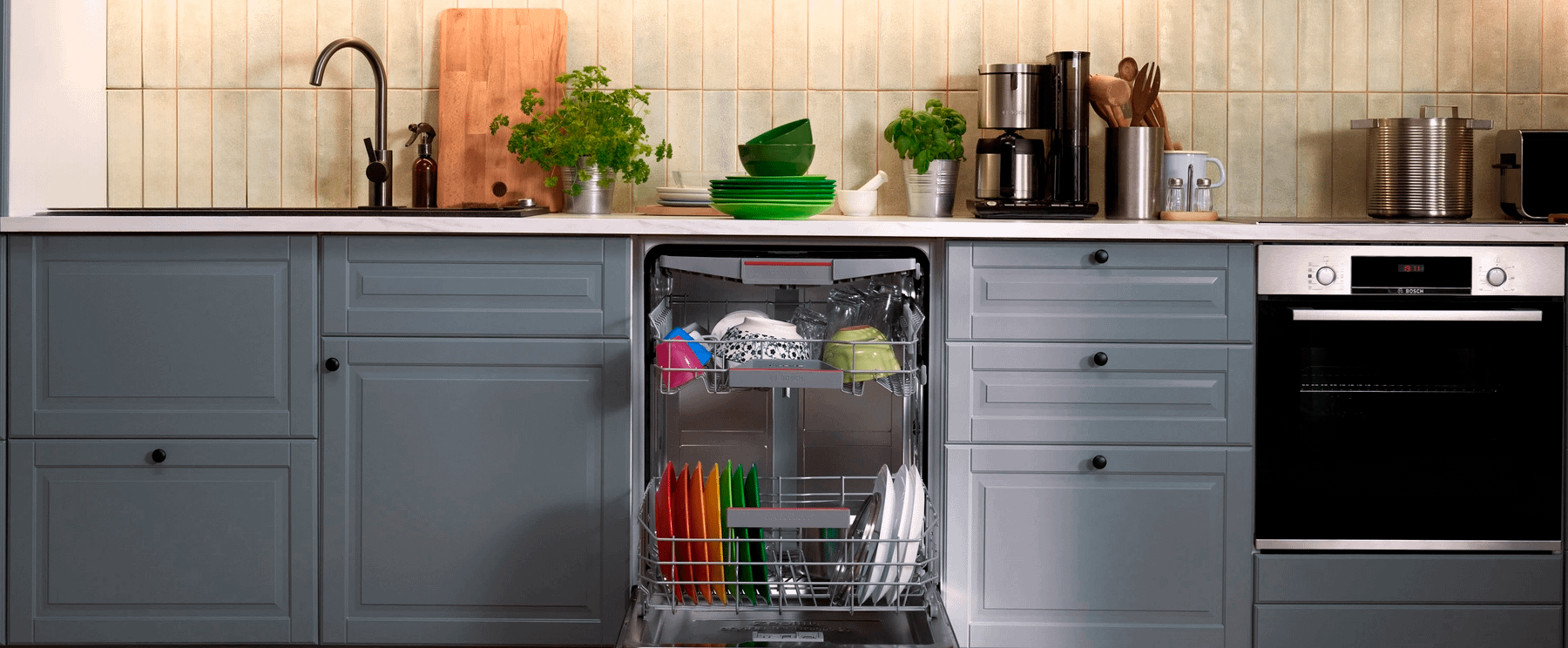 Opened dishwasher integrated into blue cabinets, with colourful plates arranged in rainbow order.