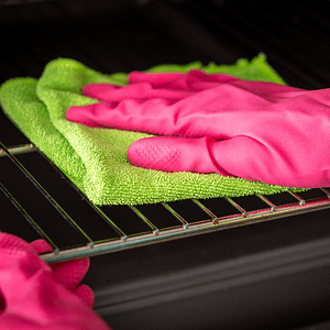 Cleaning oven using green microfibre cloth wearing pink gloves