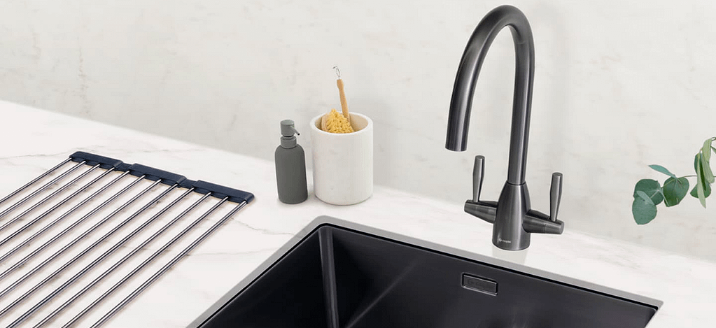 A rounded grey tap with two handles either side. Shown next to matching sink and washing up supplies.
