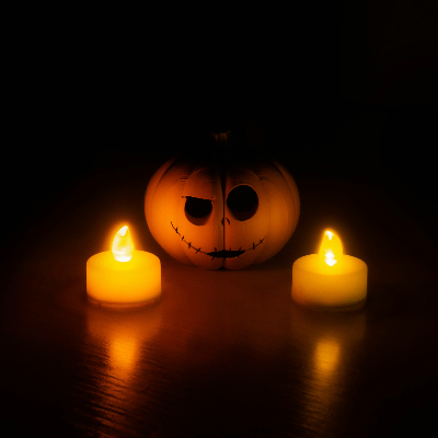 2 LED candles in front of a carved pumpkin in the dark