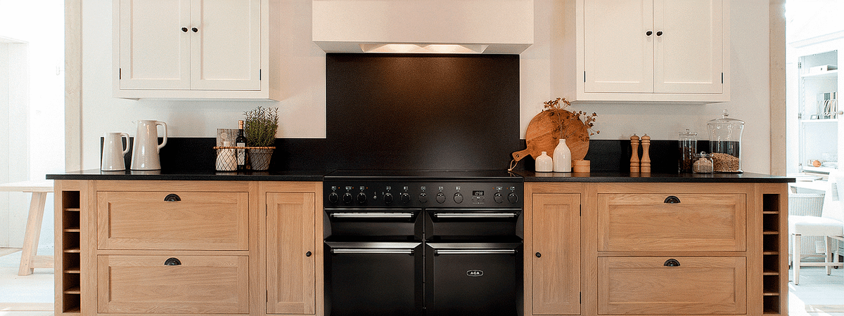 A modern black AGA range cooker installed in a kitchen with wooden cabinets and black countertop. Top cabinets and extraction fan are white.