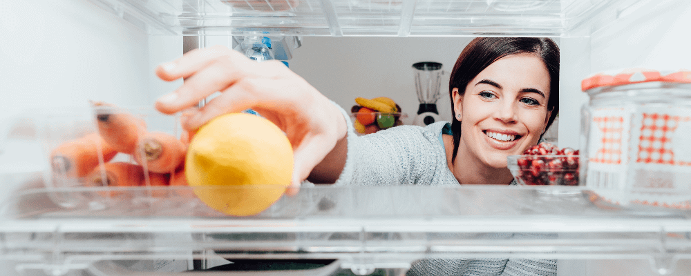 View from inside of a fridge as woman reaches in to grab a lemon
