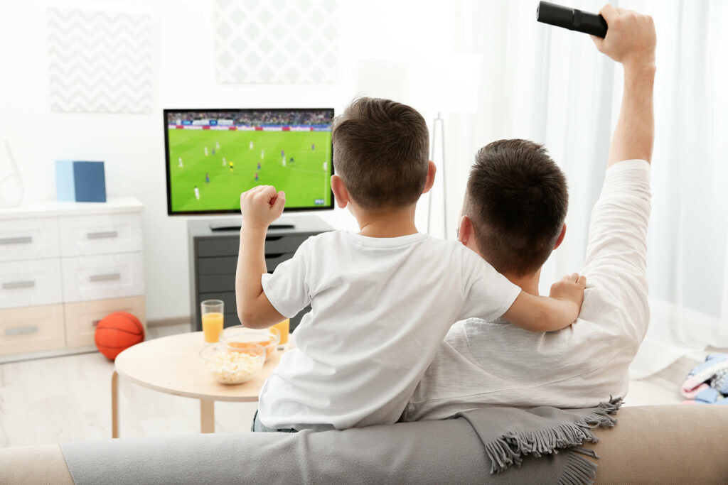 A boy and a man watching football together on their smart TV