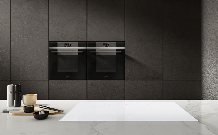 Two smeg built-in ovens side by side in a dark kitchen interior