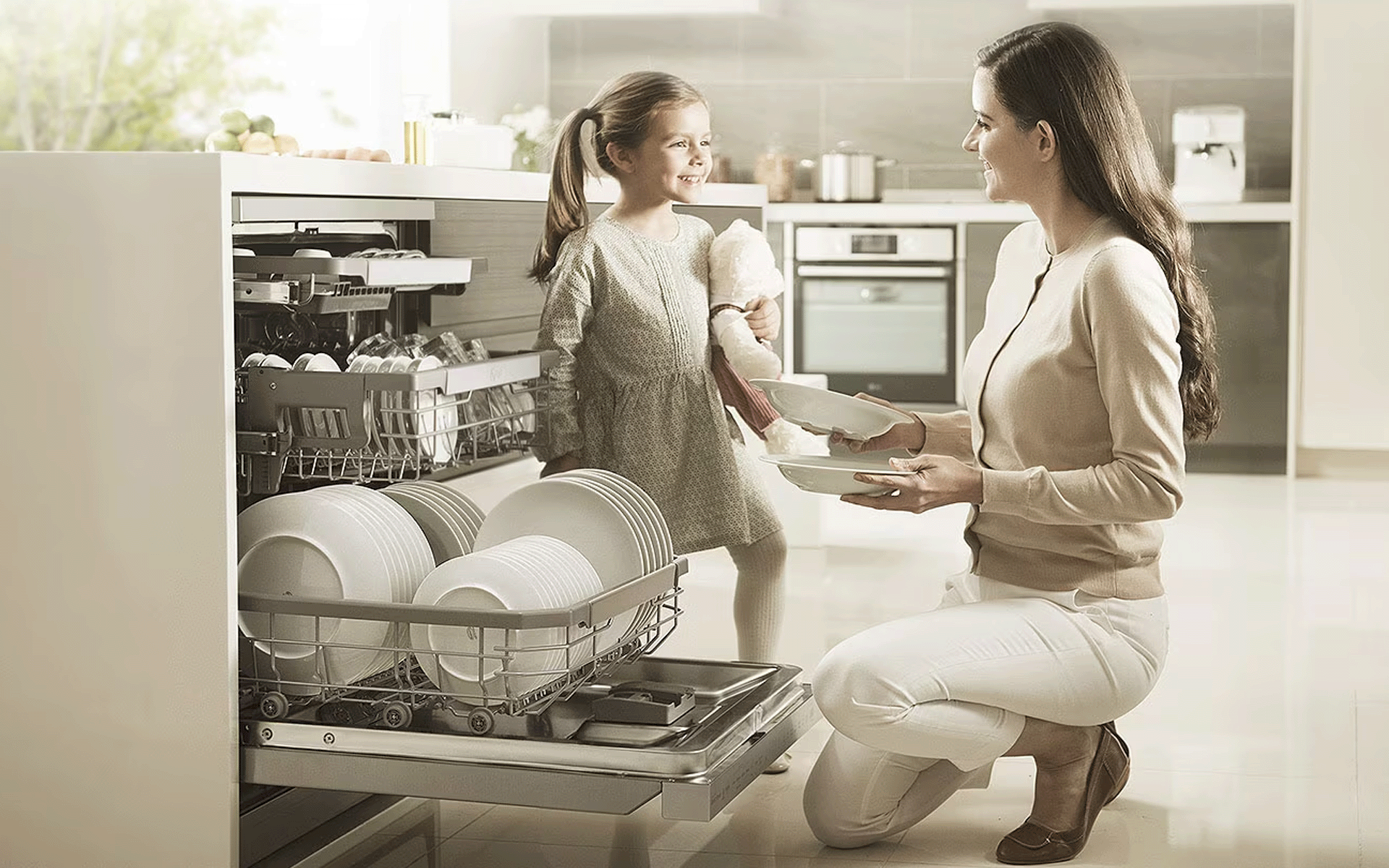 Mother kneeling down next to an open LG dishwasher, smiling at her young daughter standing next to her
