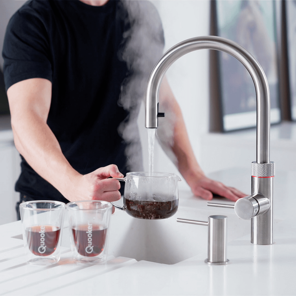 Stainless silver boiling water tap, pouring boiling water into a tea pot filled with tea