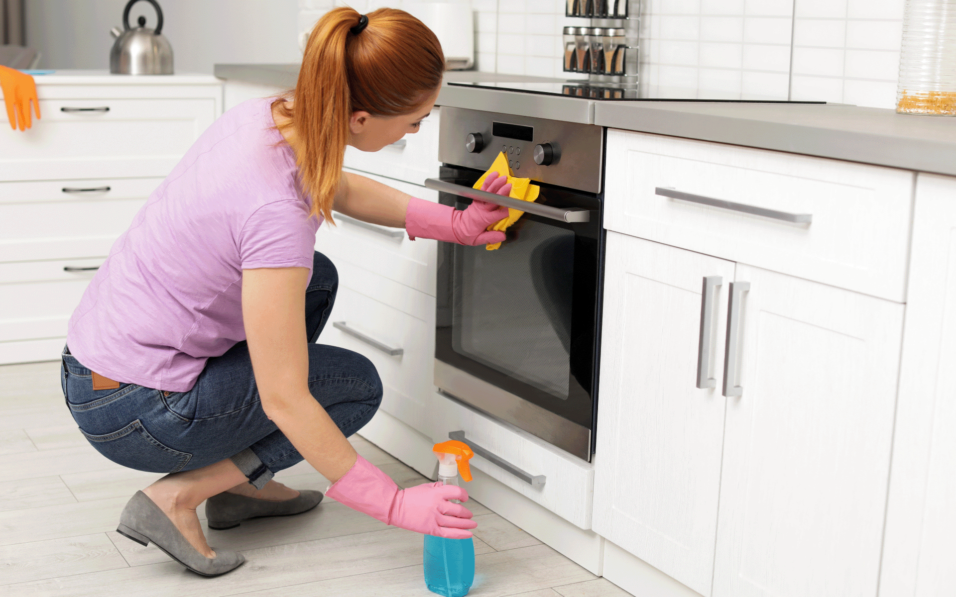 Woman in pink top and gloves cleaning the front of an oven with blue liquid.