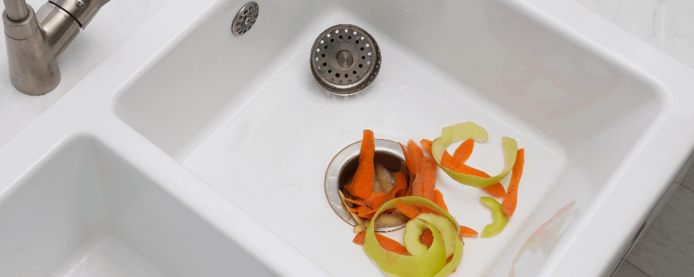 Vegetable peels shown in white sink, going into the food disposal unit.
