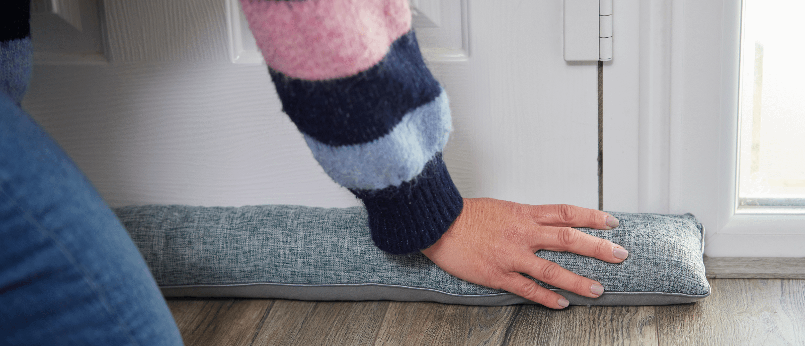Person placing a grey draught excluder against bottom of front door