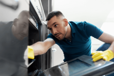 Man reaching into oven wearing yellow cleaning gloves