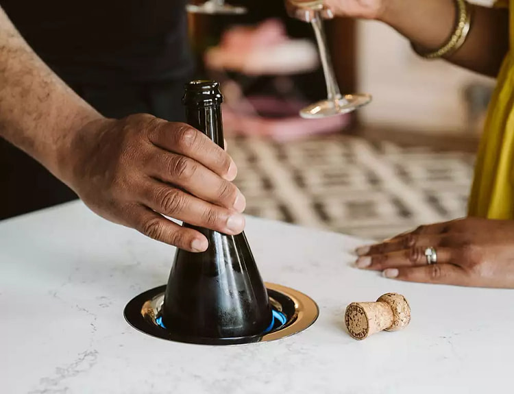 Hand pulling out a bottle of wine from a Kaelo; a wine chiller built into a countertop.