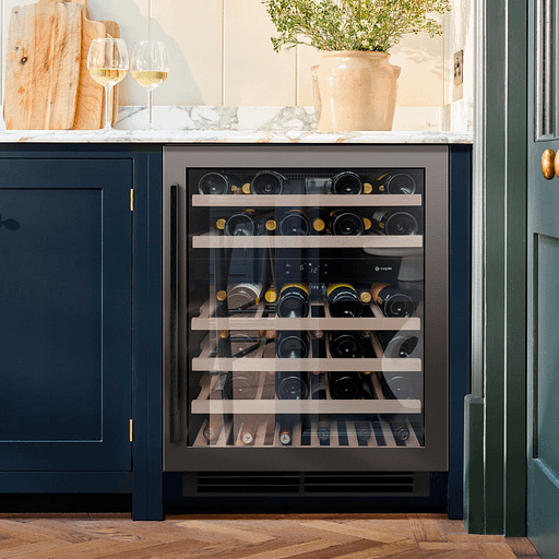A wine cooler built in under a navy blue counter, stocked full of wine bottles.