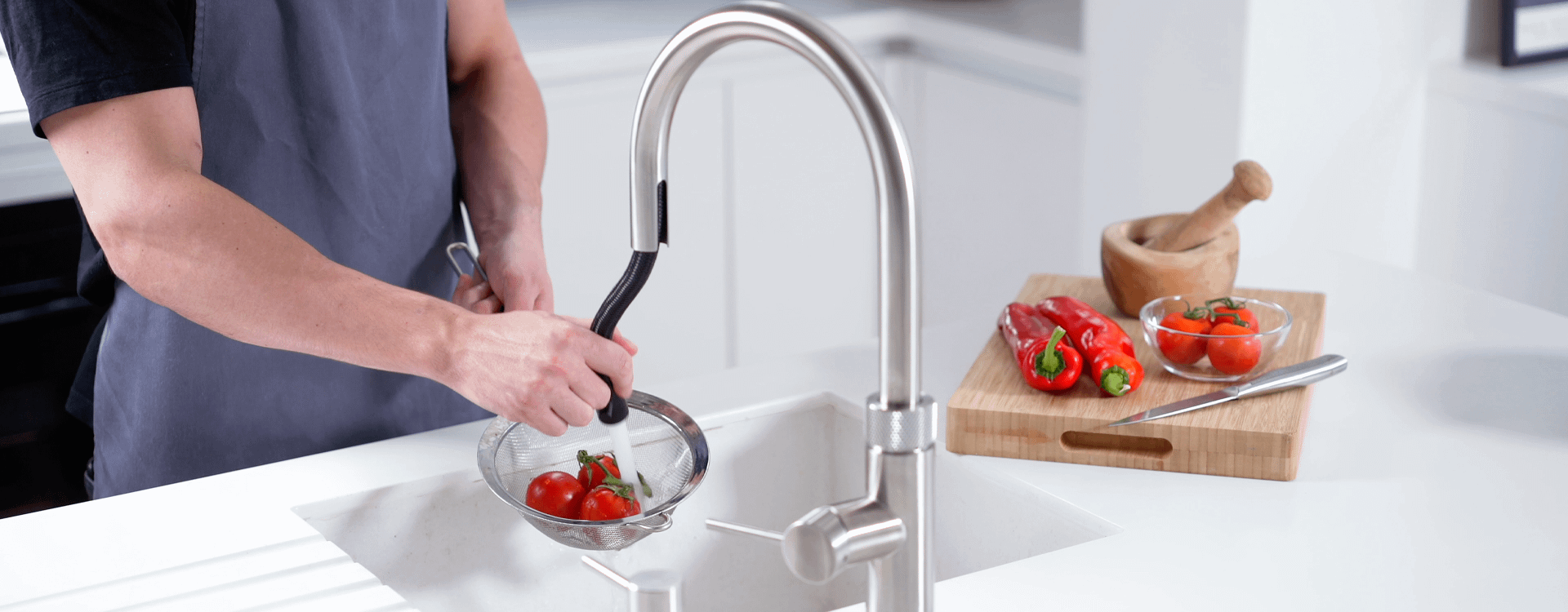 Someone washing tomatoes in a sink with a pull-out stainless steel tap