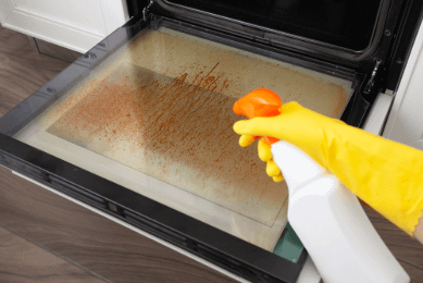 Spraying glass cleaner onto oven door