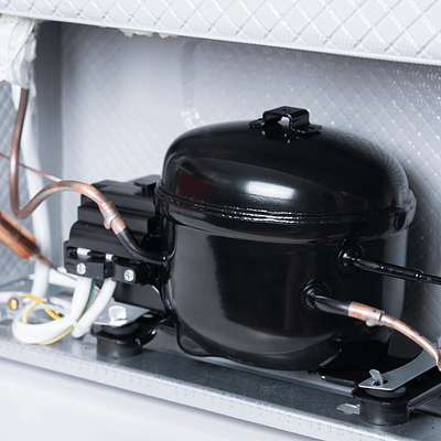 A black fridge compressor inside of a fridge, showing how a fridge works