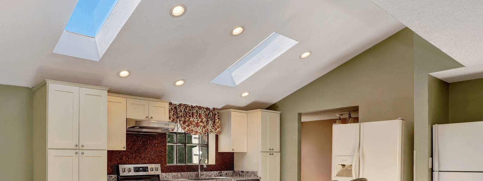 Two skylights shown above a white and green kitchen with red splashback.