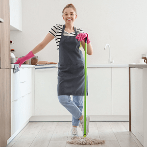 Woman standing in kitchen leaning on a mop, whilst wearing a grey apron and pink gloves