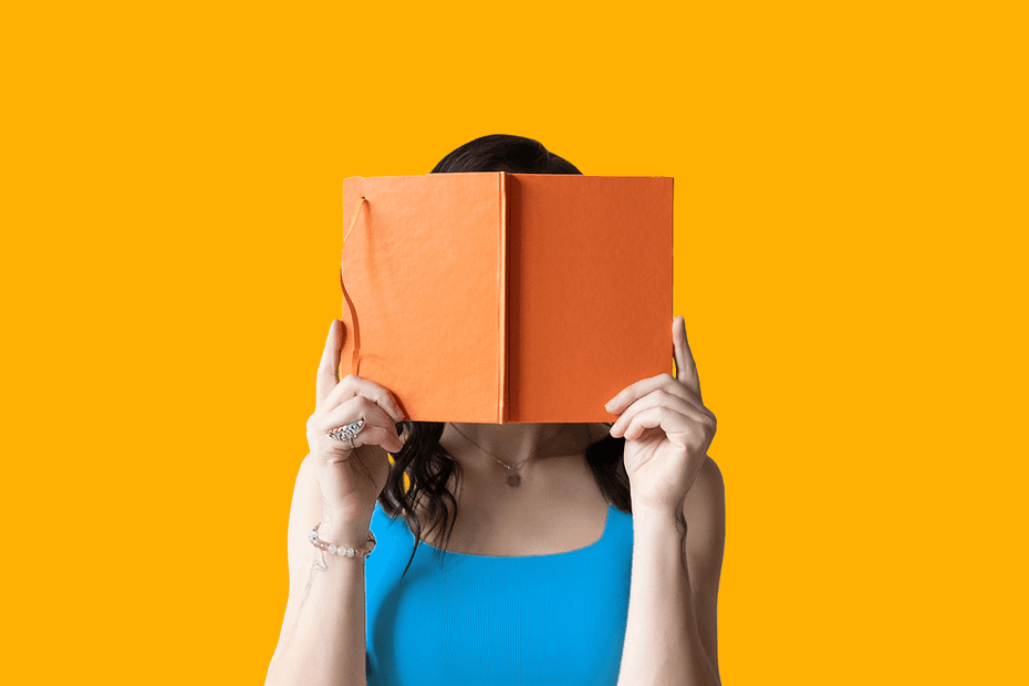 A person wearing a blue top reading an orange book, the book obscures the person's face